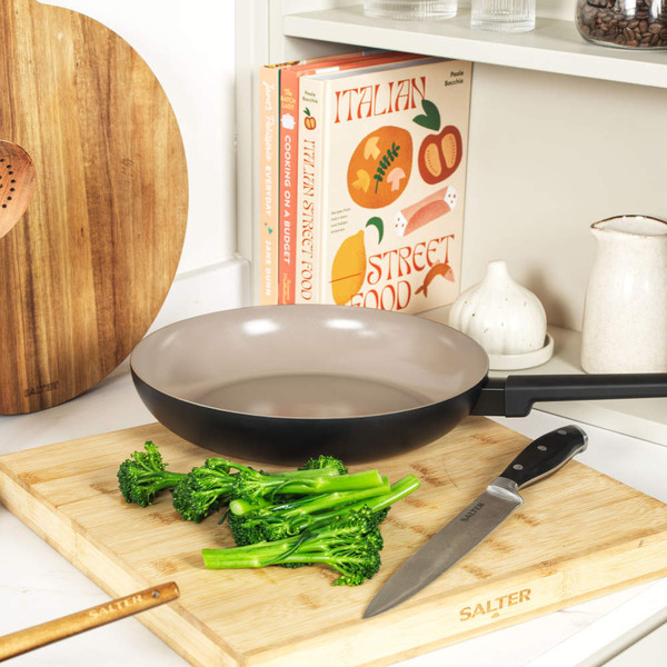 Two non-stick frying pans on an induction hob with cooked food, kitchen utensils in background