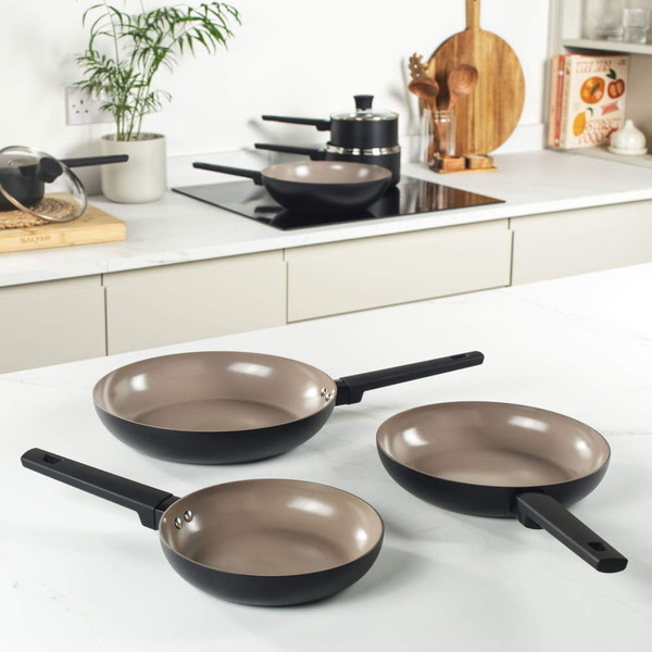 Set of three black frying pans with beige nonstick interior on kitchen worktop