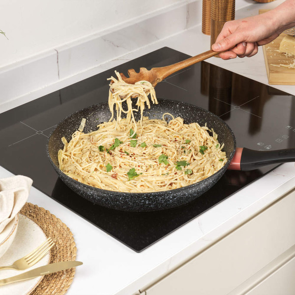 Cooked spaghetti in creamy sauce with herbs in non-stick frying pan on hob.