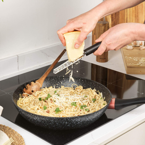 Grating parmesan cheese over cooked spaghetti in a non-stick frying pan