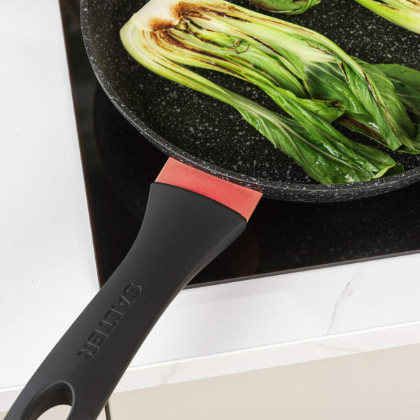 Black frying pan with red accent and two pak choi halves cooking on a modern hob