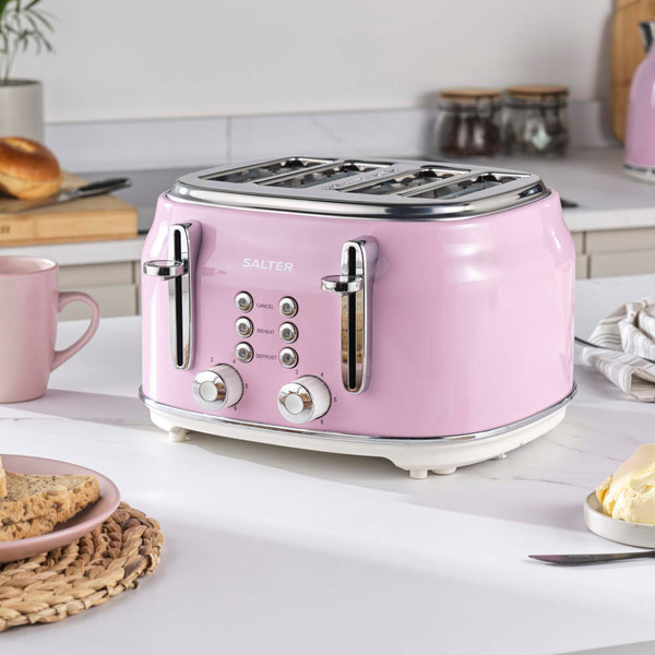Pink 4-slice toaster with crumb tray partly open, beside plate of toast and pink mug
