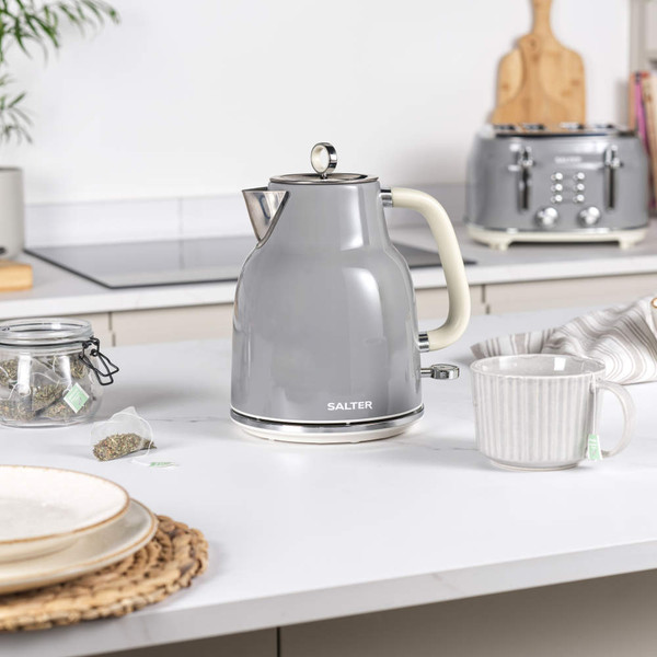 Grey electric kettle pouring hot water into matching grey mug, hand holding handle
