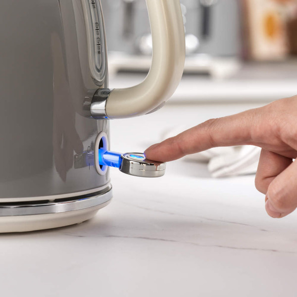 Grey electric kettle close-up, finger pressing illuminated power switch