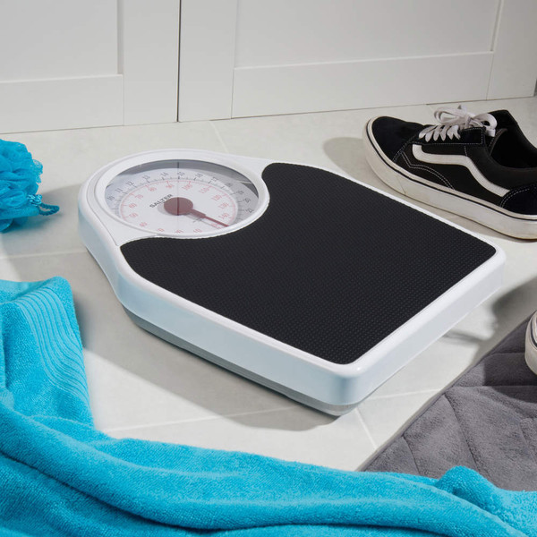 Mechanical bathroom scale with black platform, shown on floor with towel and shoes