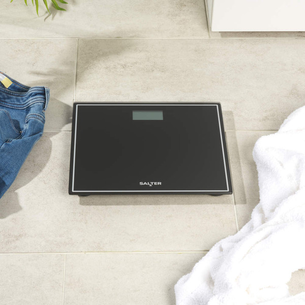 Black Salter digital bathroom scale with clear LCD display, shown on wooden floor