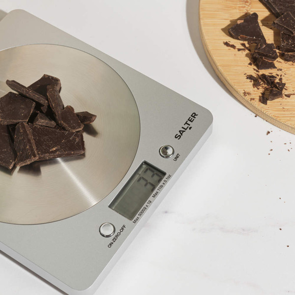 Digital kitchen scale weighing dark chocolate pieces on countertop, Salter brand visible