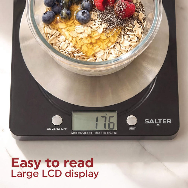 Digital kitchen scale being cleaned, surrounded by baking ingredients and cookies