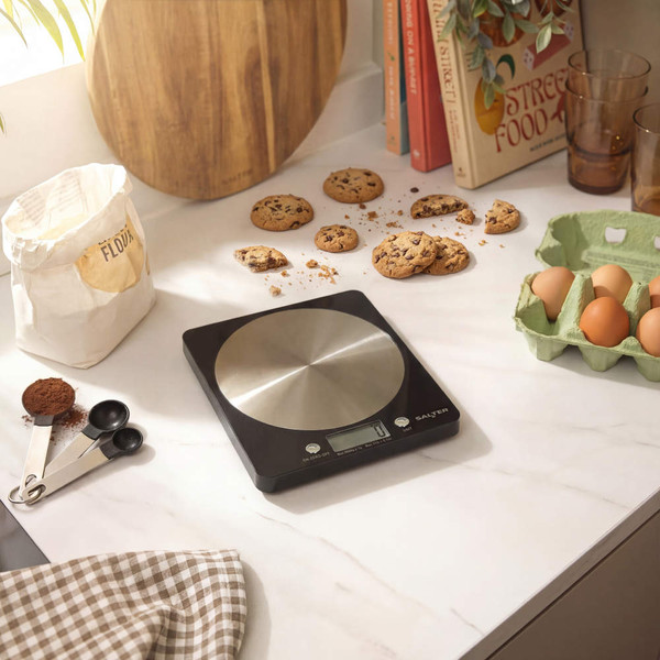 Black digital kitchen scale on worktop with baking ingredients, ideal for home cooks