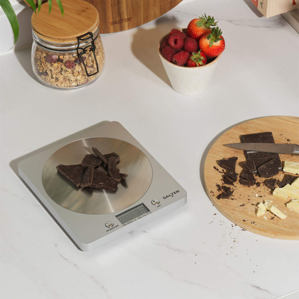 Digital kitchen scale weighing dark chocolate pieces on countertop
