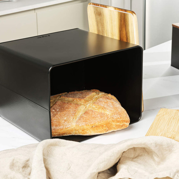 Black metal bread bin with wooden lid, shown with crusty loaf inside on kitchen counter