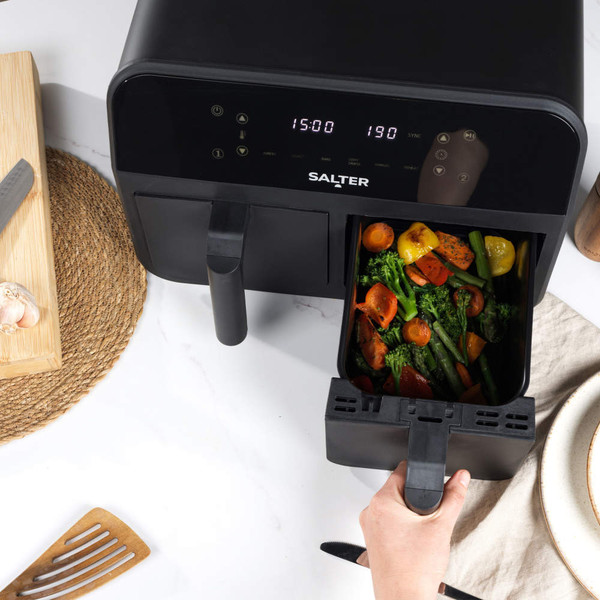 Black digital air fryer drawer opened, showing cooked mixed vegetables inside on a kitchen countertop