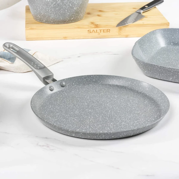 Grey frying pan on induction hob with pancake, stack of pancakes and fruit in background