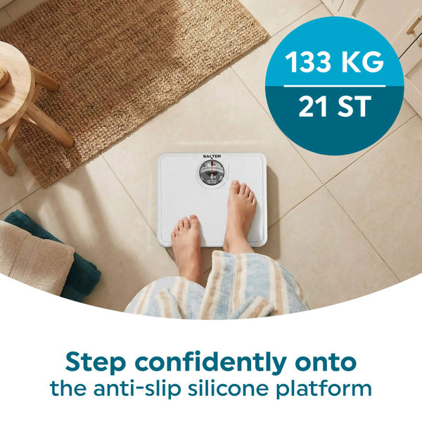 Mechanical bathroom scale in white, shown in use on tiled floor.
