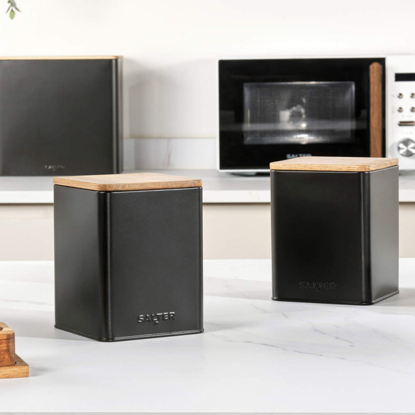 Set of two black metal storage canisters with wooden lids on kitchen worktop
