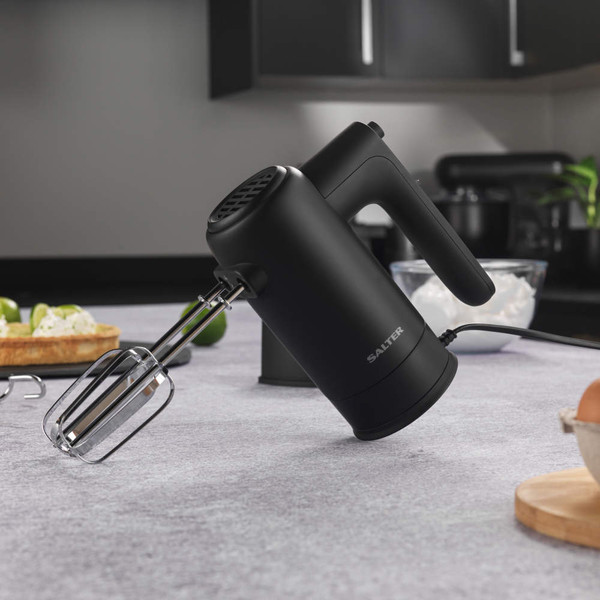 Black electric hand mixer with beaters, shown on kitchen worktop.