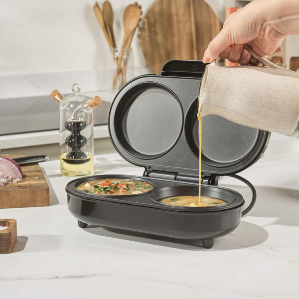 Electric omelette maker with two non-stick trays, mixture being poured in, kitchen setting