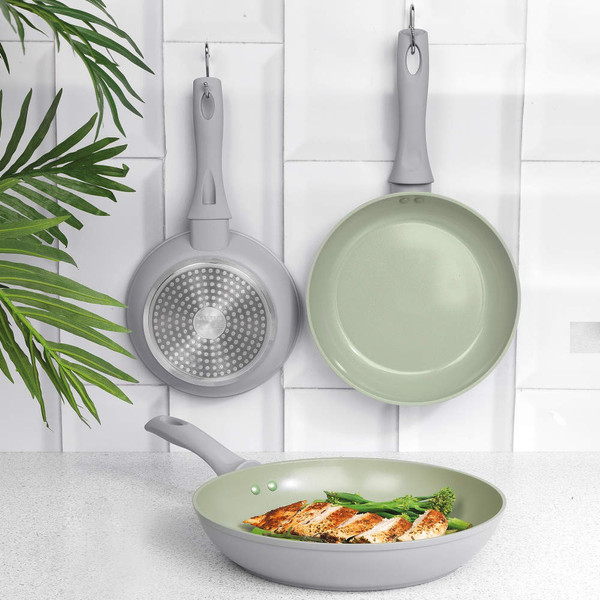 Set of grey frying pans, one cooking chicken and broccoli, shown on kitchen counter.