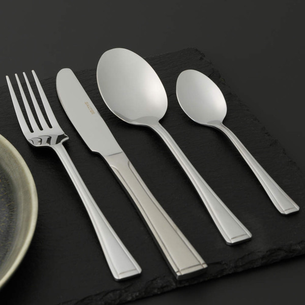 Set of four stainless steel cutlery pieces on wooden table: knife, fork, spoon, teaspoon.