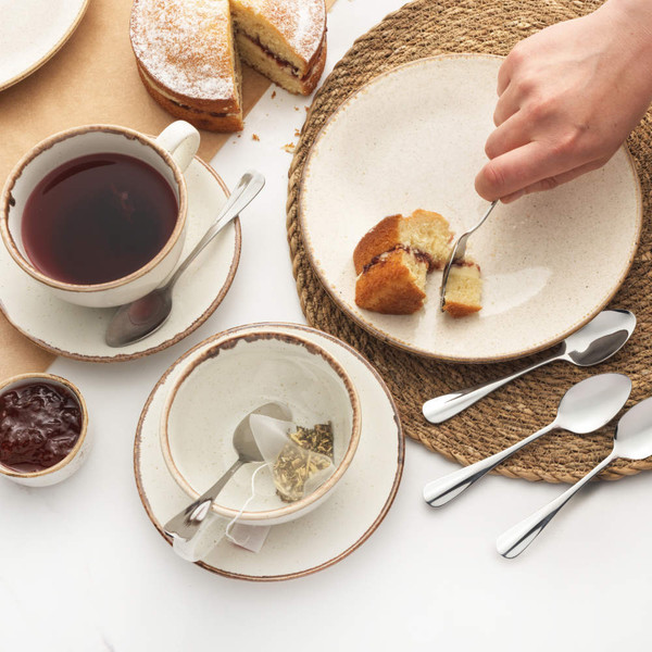 Table setting with cake, tea, ceramic crockery and stainless steel teaspoons.