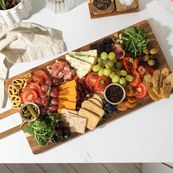 Wooden serving board with assorted cheeses, cured meats, fruit, crackers and chutney
