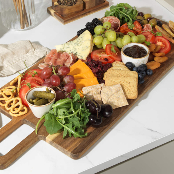 Wooden serving board with assorted cheeses, cured meats, fruit, crackers and chutney