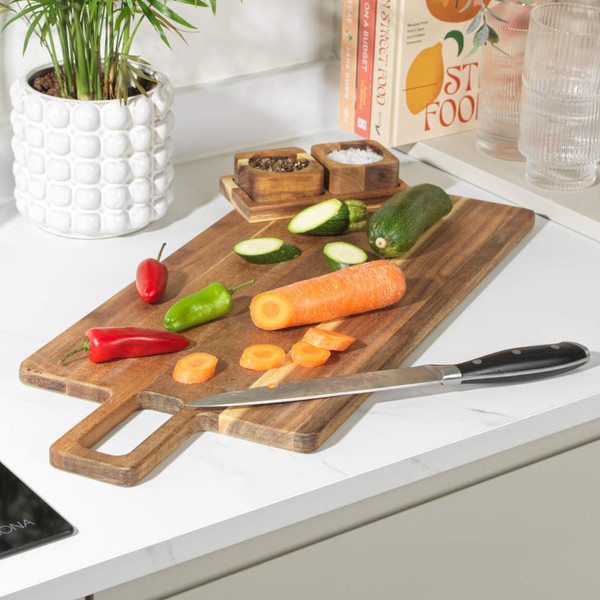 Wood chopping board with knife, carrot, courgette and chillies on white kitchen worktop