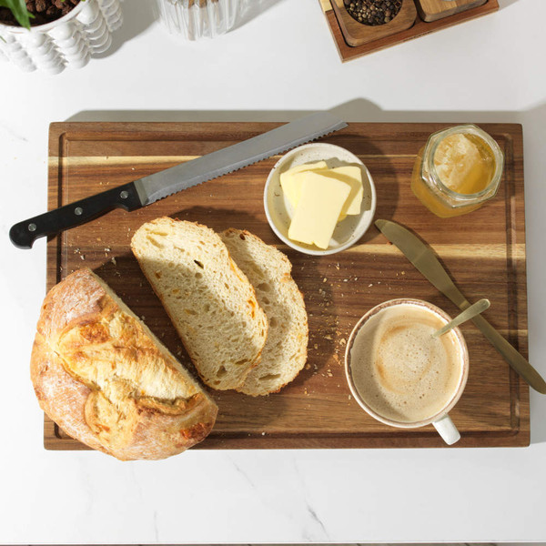 Sliced crusty loaf with butter, honey, and coffee on wooden board, breakfast set.