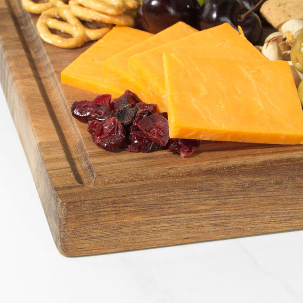 Sliced cheddar cheese with dried cranberries, green olives and pretzels on a wooden board.