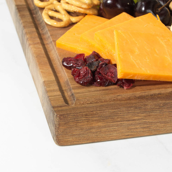Sliced cheddar cheese with dried cranberries, green olives and pretzels on a wooden board.