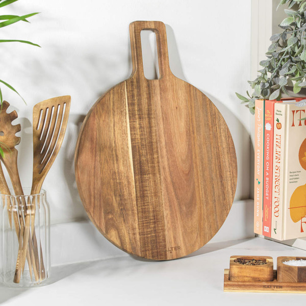 Round wooden chopping board with handle, shown upright on kitchen counter.