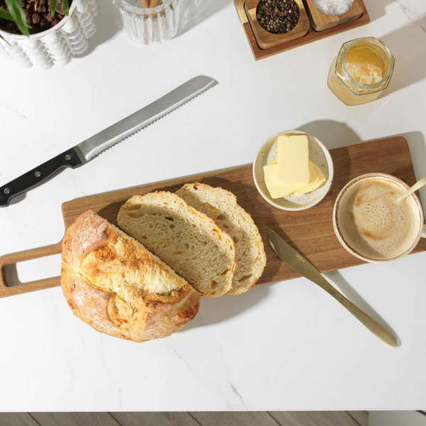Sliced rustic loaf on wooden board with butter and coffee, shown for serving suggestion.