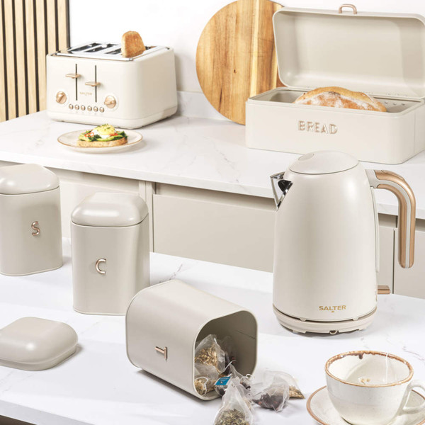 Cream metal bread bin with lid open, showing a rustic loaf inside on a kitchen counter