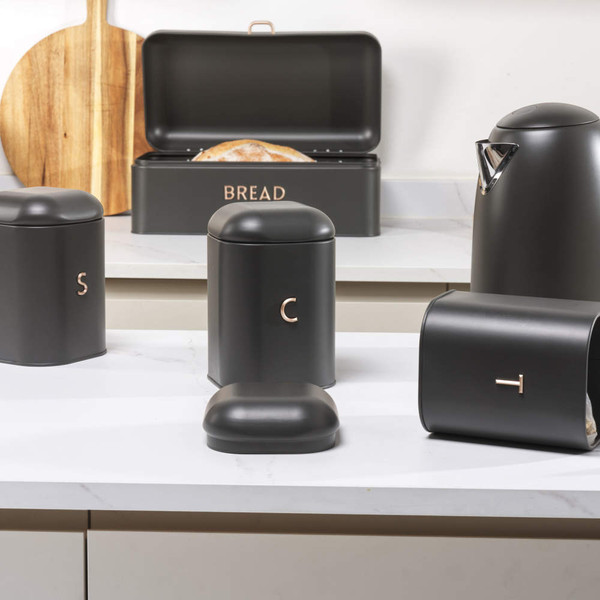 Matte black bread bin with copper lettering, open to show a loaf on a kitchen worktop