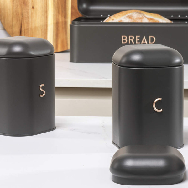 Black kitchen storage tins for salt, coffee, and bread, with metallic lettering.