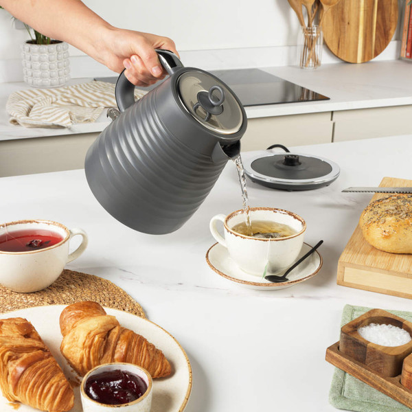 Grey electric kettle pouring hot water into matching mug, shown in use.