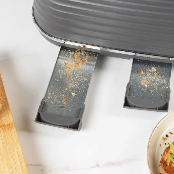 Close-up of grey toaster with two crumb trays partially open showing crumbs