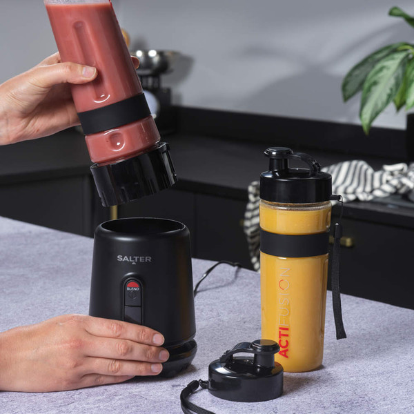 Black Salter smoothie maker with red and orange drinks in bottles on a kitchen counter