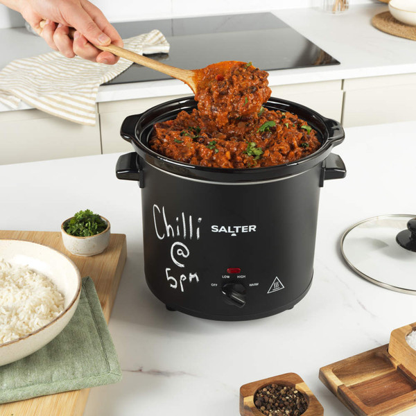 Black Salter slow cooker with glass lid, front controls and side handles on white background