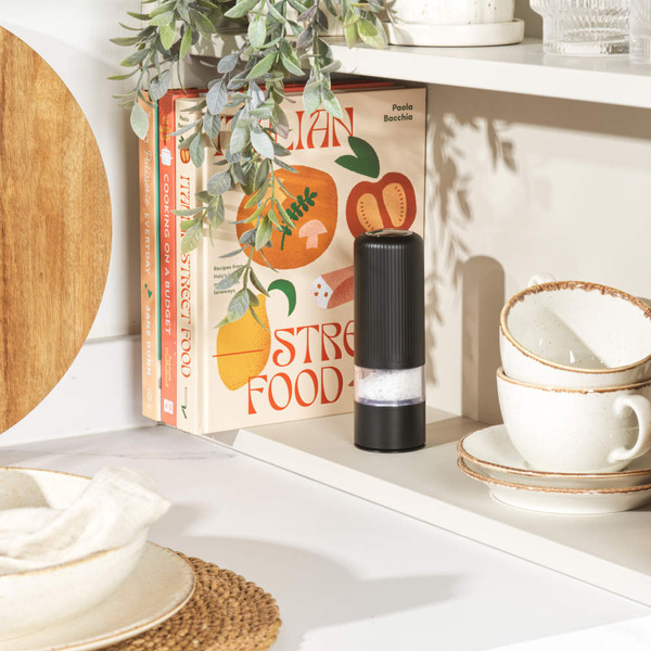 Black electric salt or pepper grinder on kitchen shelf beside cookbooks
