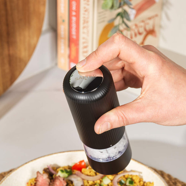 Black electric salt or pepper mill on kitchen shelf beside cookbooks and cream ceramic tableware