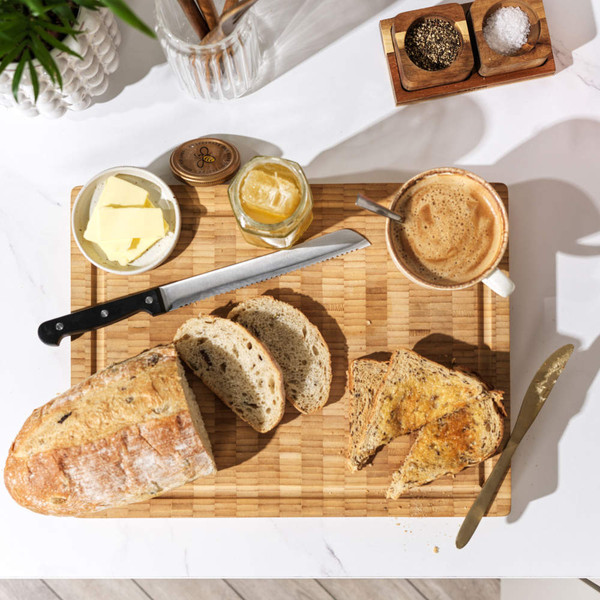Breakfast setup: sliced rustic bread, butter, honey, and coffee on wooden board
