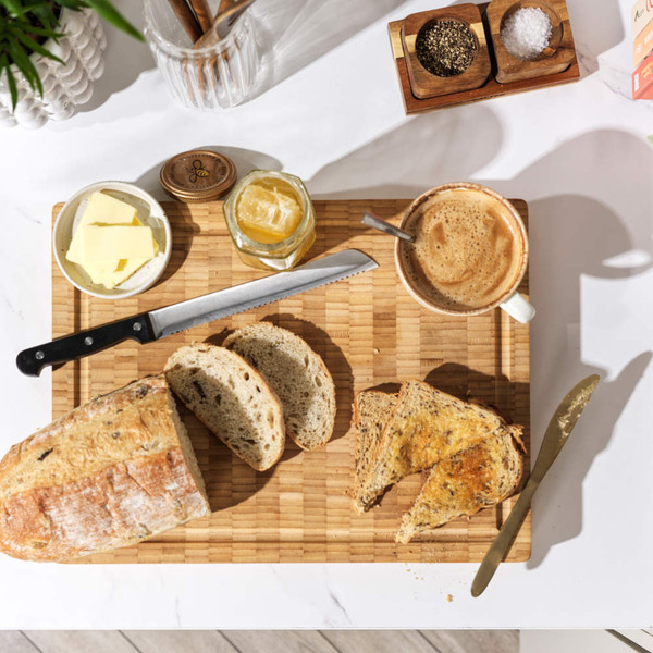 Breakfast setup: sliced rustic bread, butter, honey, and coffee on wooden board