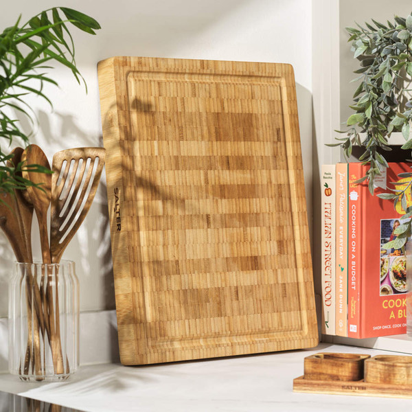 Large rectangular bamboo chopping board with groove, upright on kitchen worktop