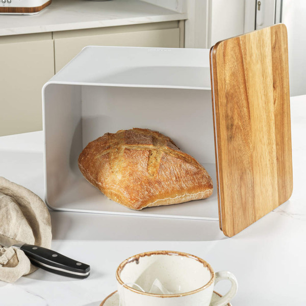 White bread box with wooden lid holding a round crusty loaf on kitchen worktop