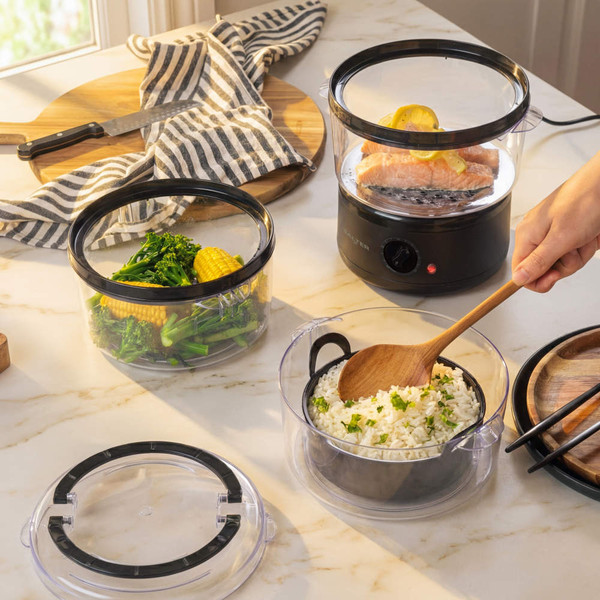 Electric food steamer in use with salmon and vegetables inside, kitchen counter setting