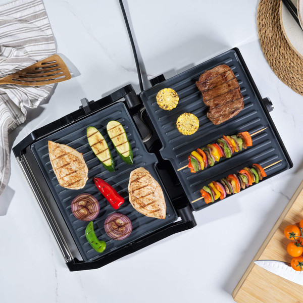 Electric grill with chicken, steak, skewers and vegetables cooking, shown open on kitchen counter
