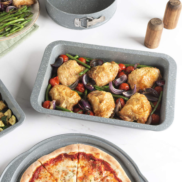 Non-stick roasting tin with cooked chicken, green beans, tomatoes and onions on a white background
