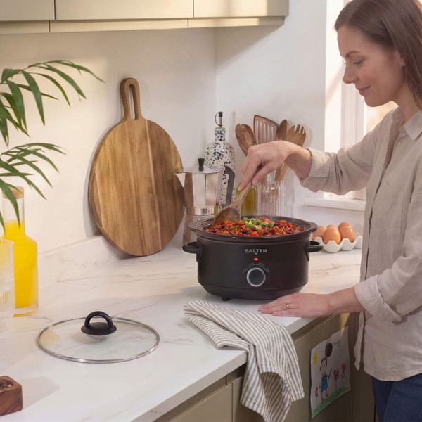 Black Salter slow cooker on kitchen counter, lid being lifted to show cooked meal