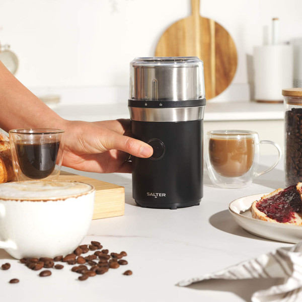 Electric coffee grinder, black and silver, shown in use on kitchen counter